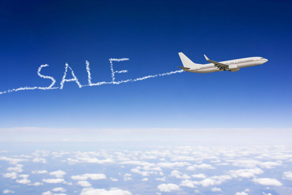 Airplane flying through the sky with word "Sale" written in the clouds.